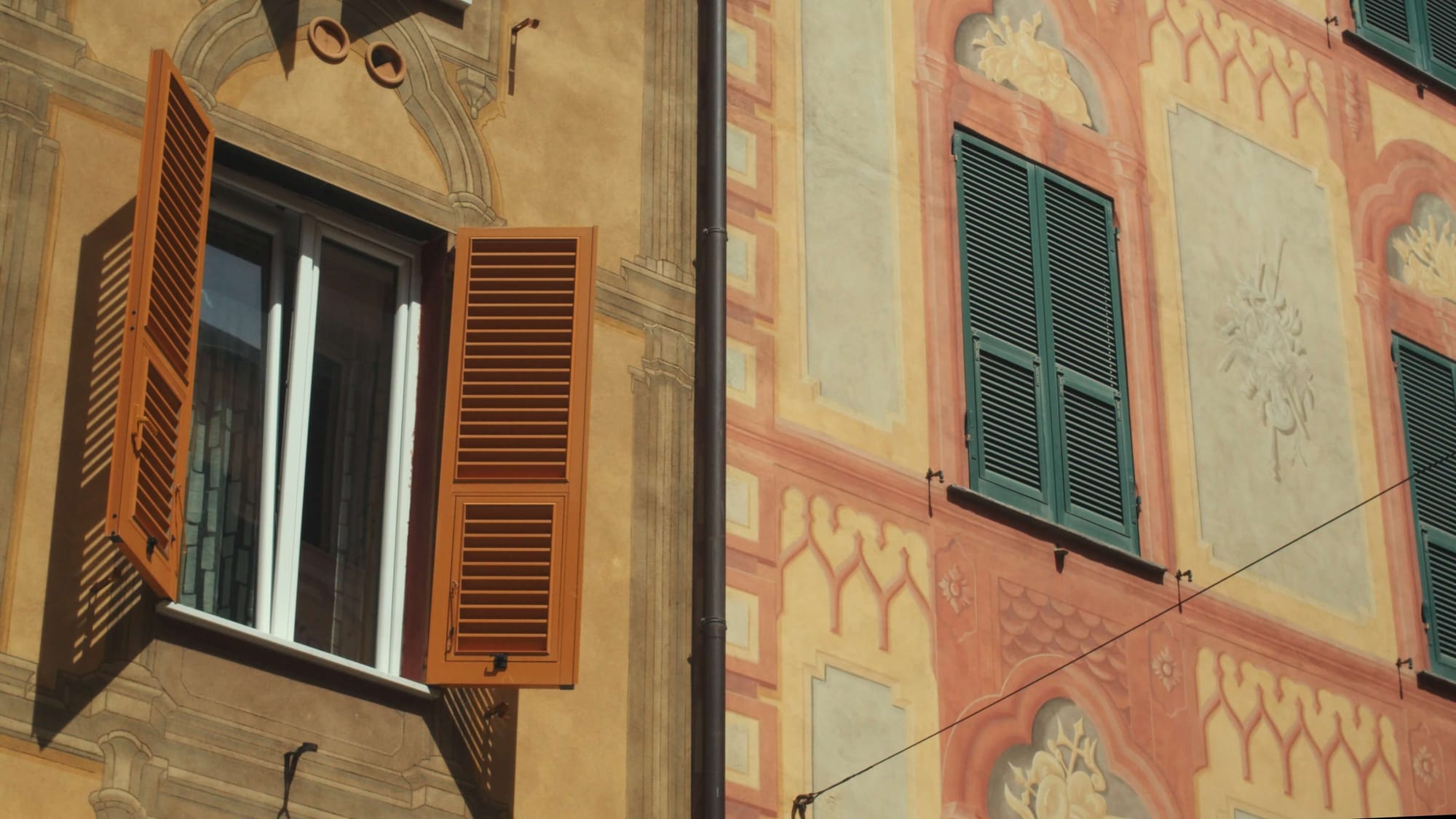 Trompe-l’œil façades in sun-washed ochres and corals frame open shutters in Liguria