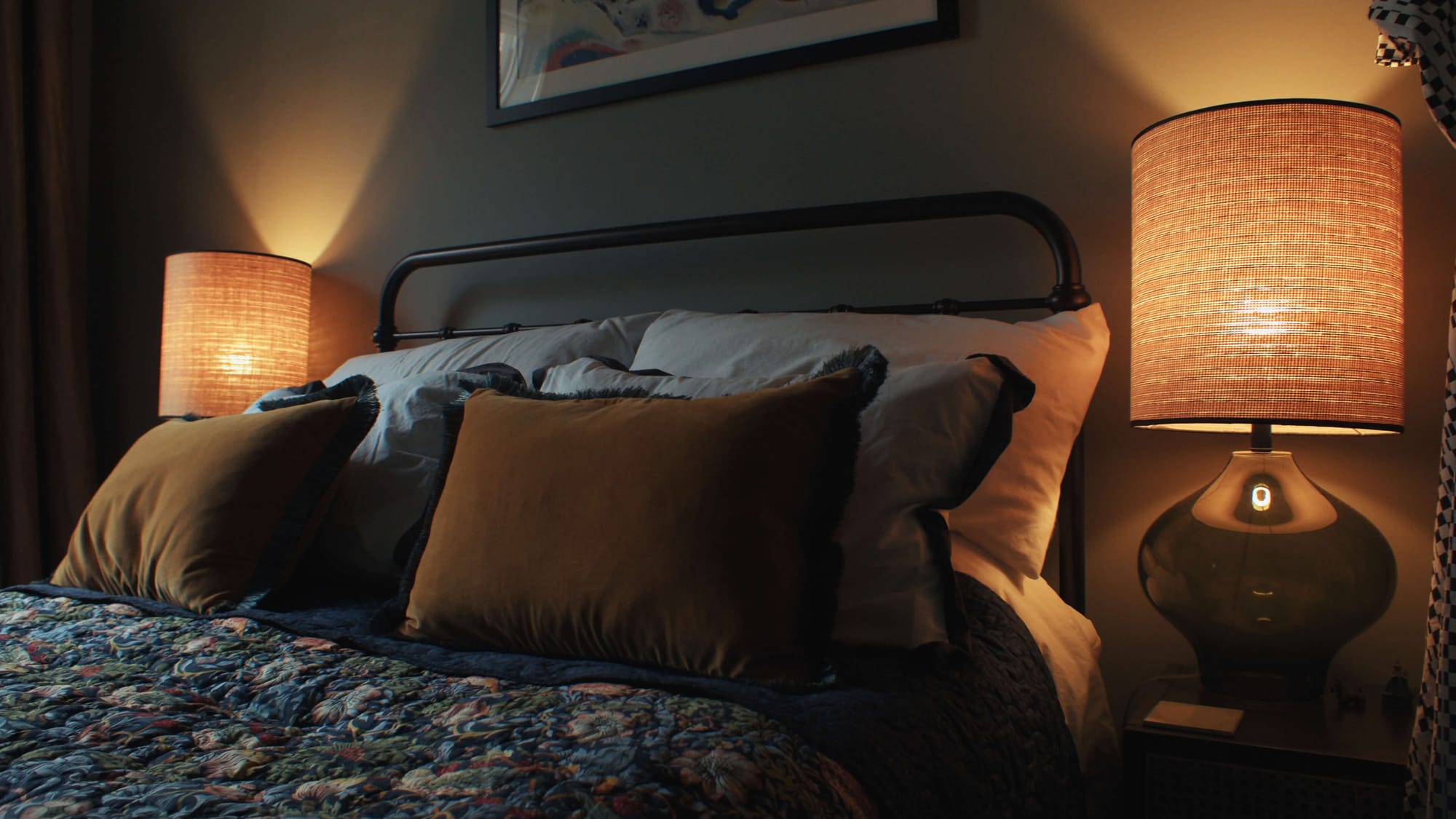 Moody bedroom with warm bedside lamps, layered bedding, and mustard velvet cushions creating a cosy atmosphere