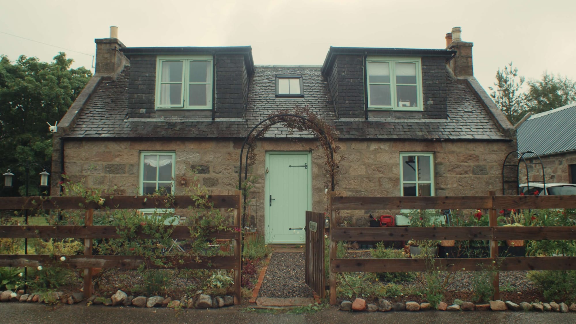 Stone farmhouse with slate roof, pale green front door and small fenced garden