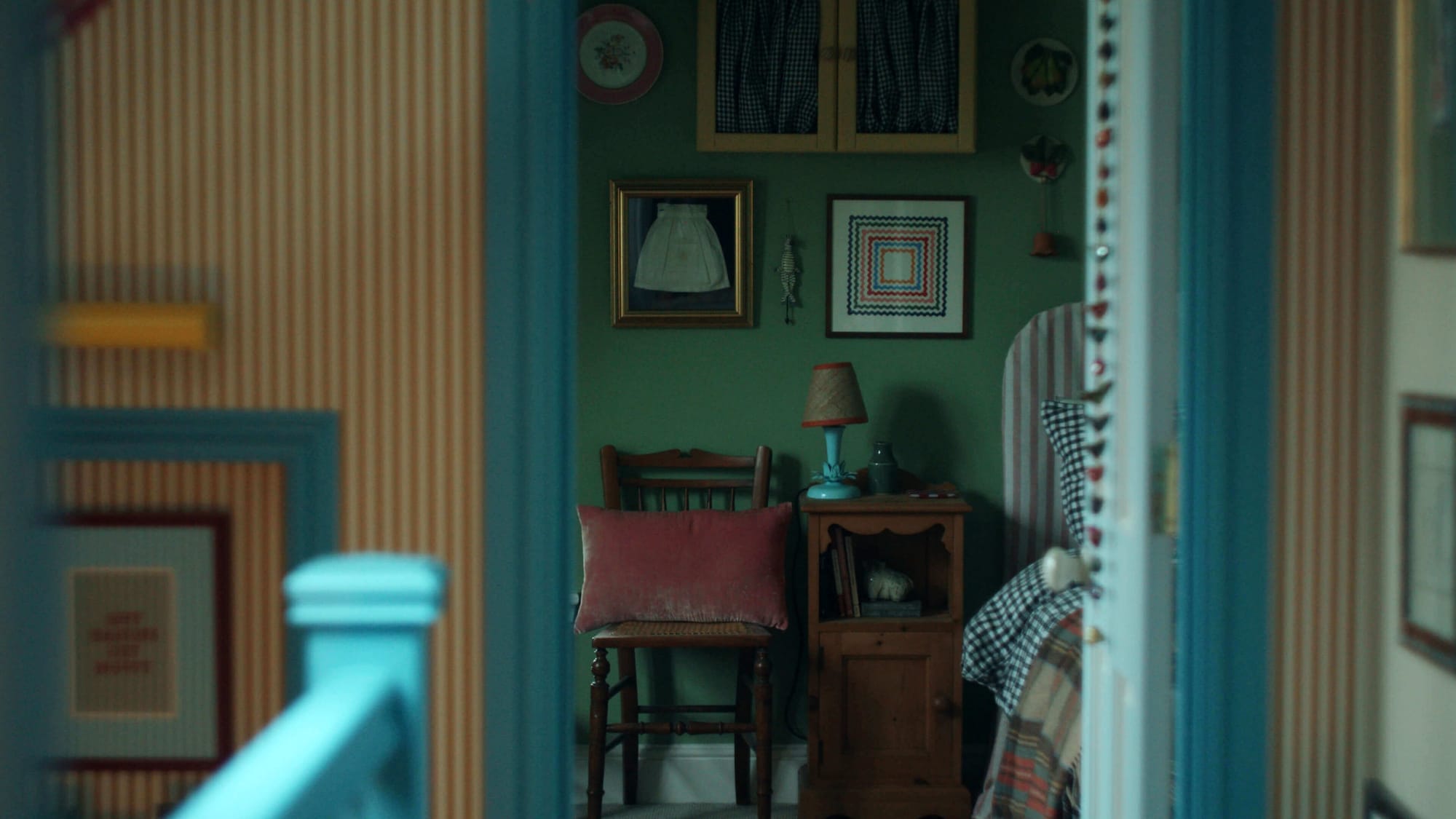 Small bedroom with green walls, wooden chair, bedside table, patterned bedspread and framed artwork