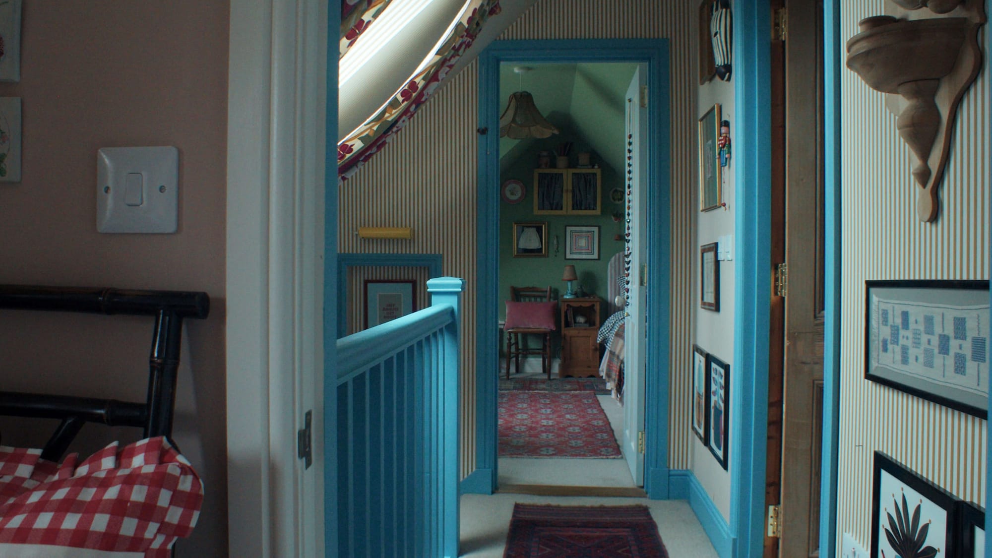 Narrow upstairs hallway with striped wallpaper, blue-painted woodwork, framed pictures and a view into a small bedroom