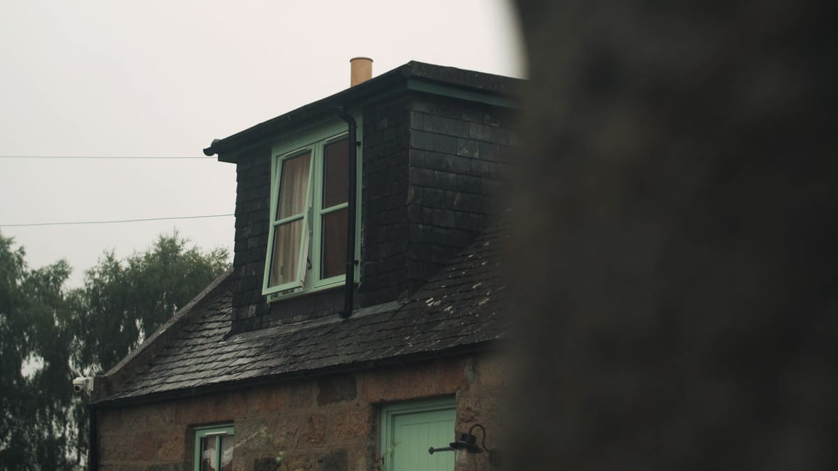 Stone cottage with dark slate roof and a small dormer window with pale green frames