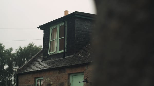 Stone cottage with dark slate roof and a small dormer window with pale green frames